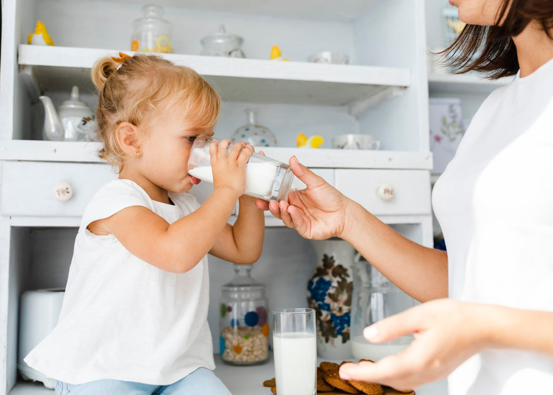 una mamma tiene un bicchiere di latte per aiutare la figlia a bere